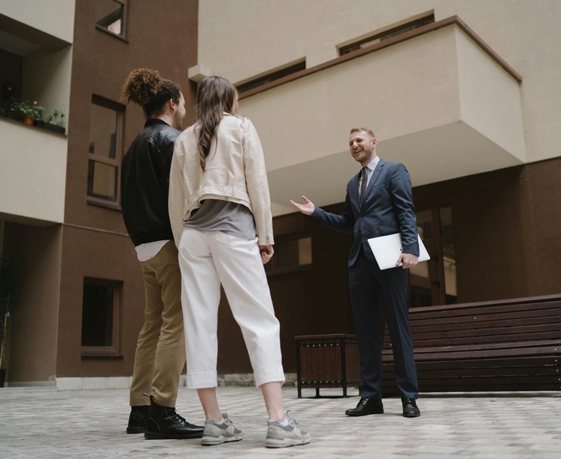 Uśmiechnięty doradca nieruchomości stający przed budynkiem rozmawiający z klientami